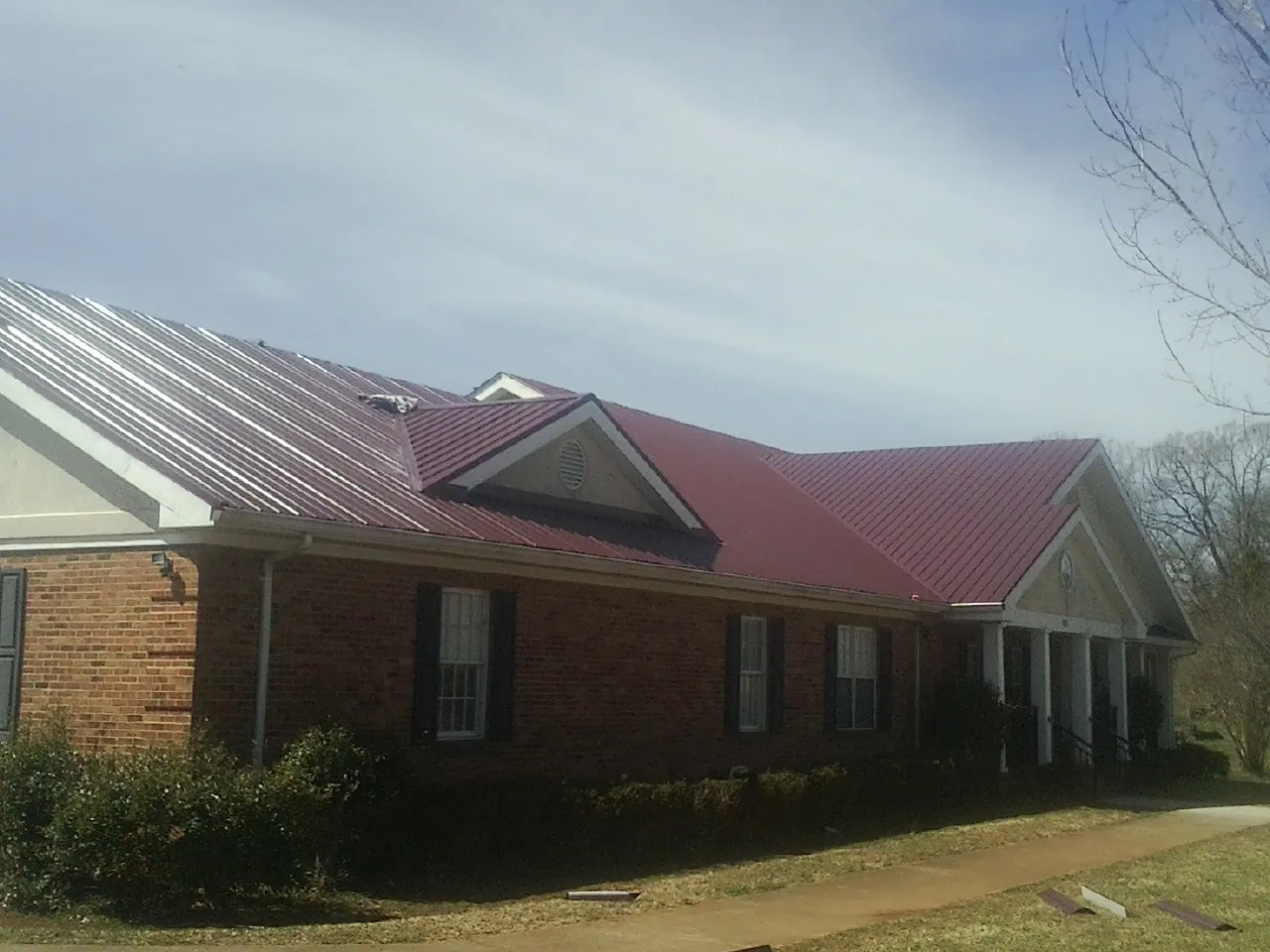 Red metal roof with gabled entries on a long brick building, from a Hail Damage Roof Repair job in Baltic