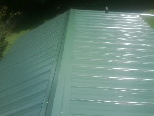 New green metal panels meeting at the ridge of a roof — Flat Roof Repair work by our crew in Baltic