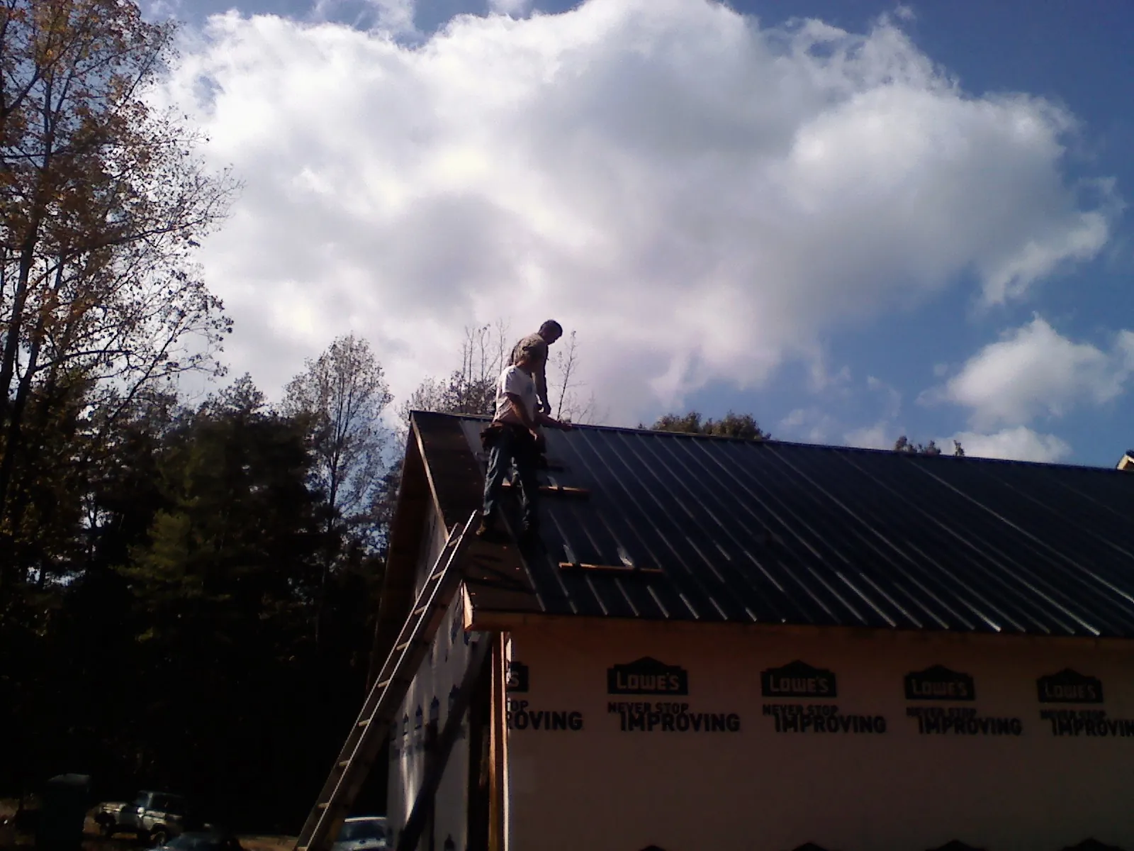 Roofer fastening dark metal panels high against a cloudy sky, from a Roof Inspection job in Baltic