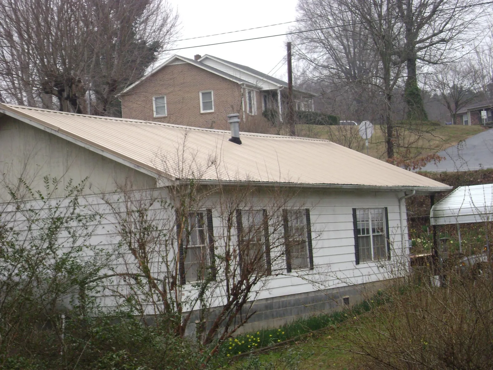 Tan metal roof on a white sided house set into a hillside — Commercial Roofing by Roofing Brothers in Baltic