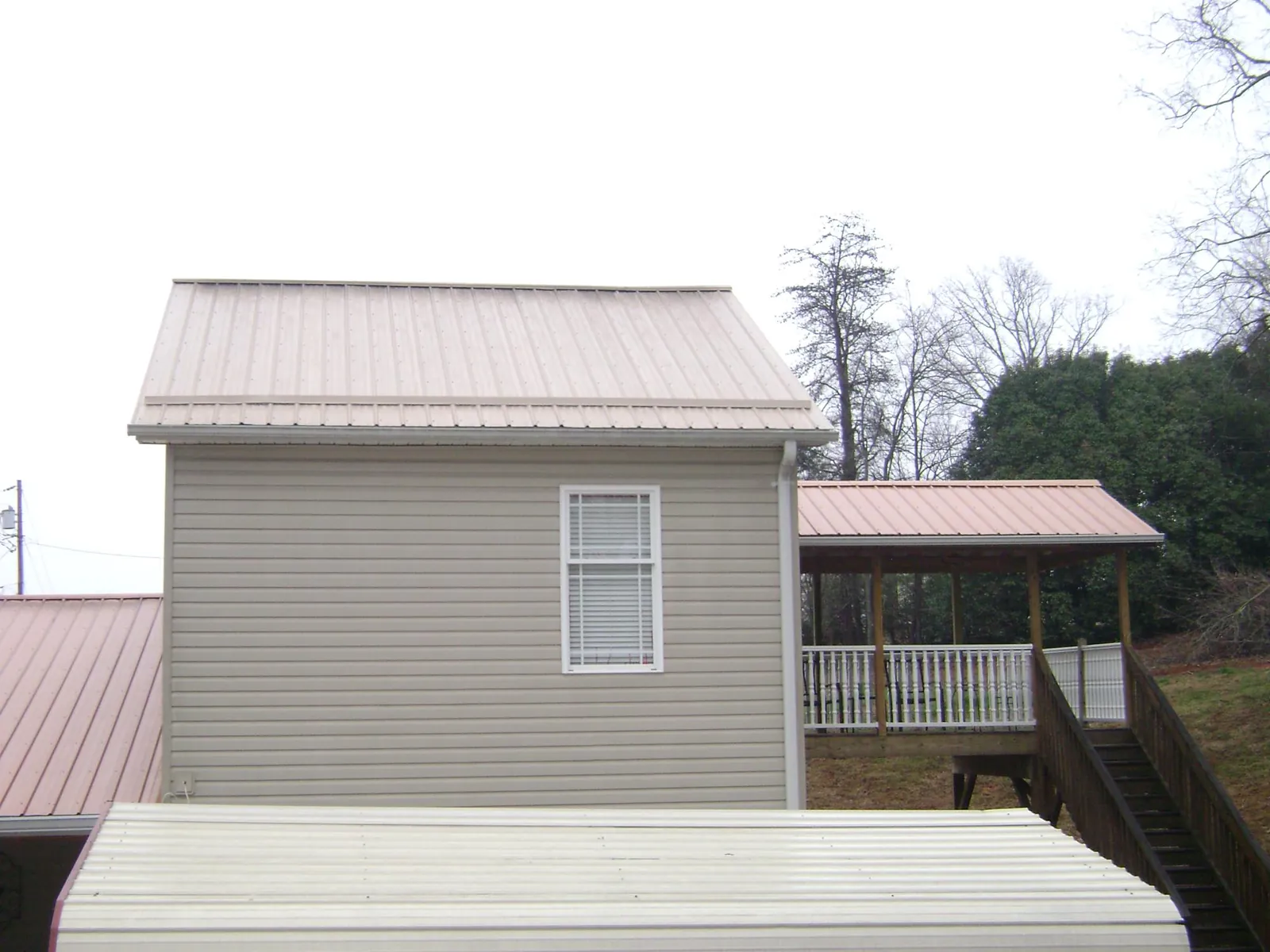 Tan metal roofs on a two story addition and attached porch, from a Roof Replacement job in Baltic